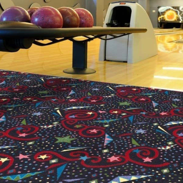 Joy Carpets Astro Jam Carpet — dark blue nylon carpet with red swirls, stars, and colorful geometric patterns in a bowling