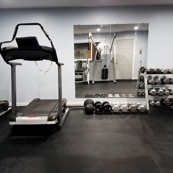 Black rubber gym mats in a home gym with cardio and strength training machines and dumbbells.