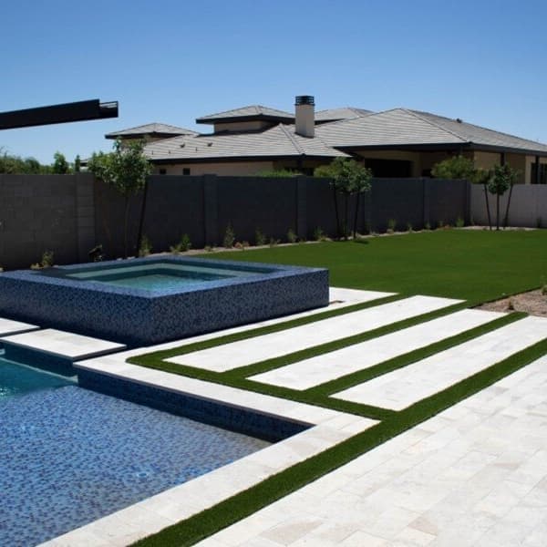 Artificial turf rolls in a residential backyard with a pool and hot tub.