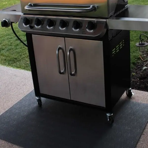 Black utility mat under a stainless steel grill on a textured patio surface