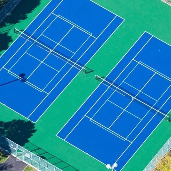Two tennis courts with navy blue playing surfaces and green surrounds, aerial view