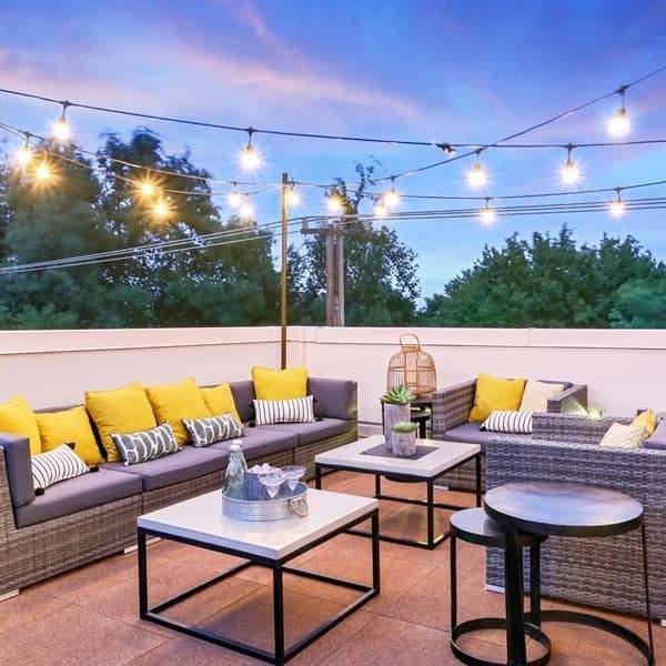 Rooftop deck with interlocking rubber tiles in brown, furnished with wicker seating and string lights at dusk