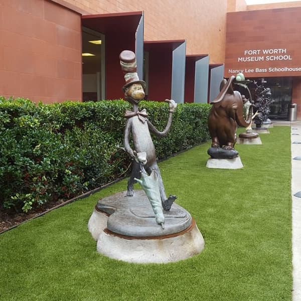 Artificial turf rolls in front of a school museum with different non-fiction character statues.