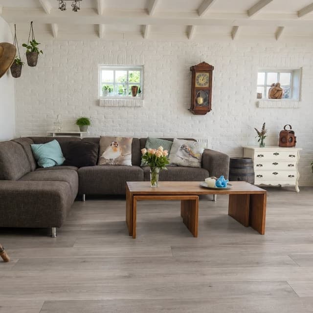 Light wood-look plank flooring in a bright living room with white brick walls, a charcoal sectional and a wooden coffee table.