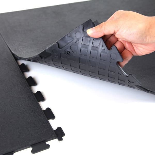 Smooth Flex Tiles, black — flexible PVC garage floor tile being bent to show interlocking edges and textured underside