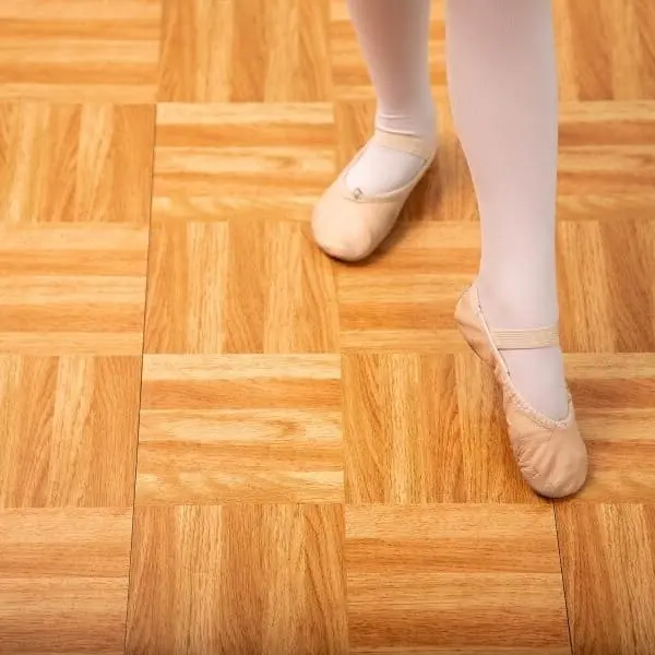 Practice Dance Tiles, light wood — dancer’s feet in ballet slippers on interlocking wood-pattern flooring