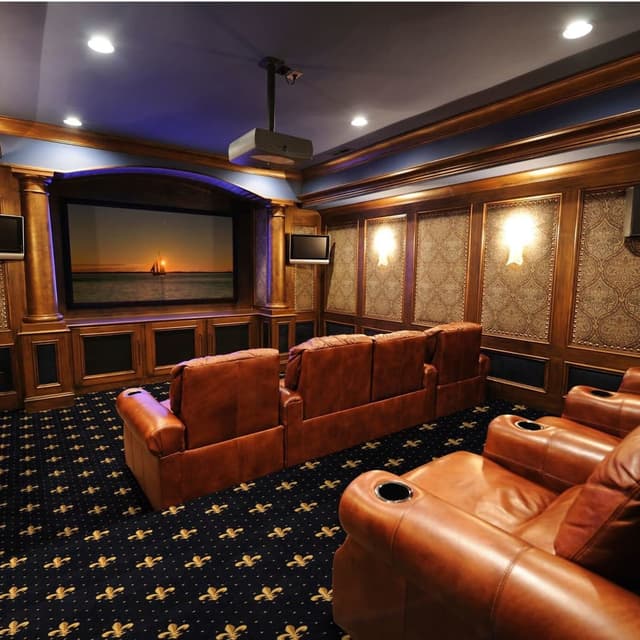 Home theater with navy carpet featuring gold fleur-de-lis pattern under leather recliners