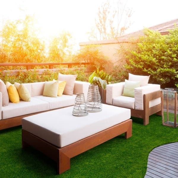 Outdoor patio with wooden furniture and a green artificial grass rug under a sofa and coffee table