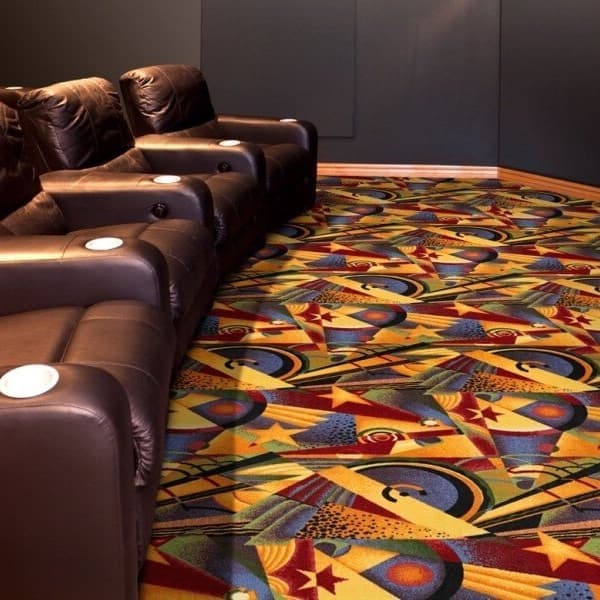Joy Carpets Sunset Strip Carpet — vibrant geometric pattern in green, orange, and yellow under recliners in a home theater