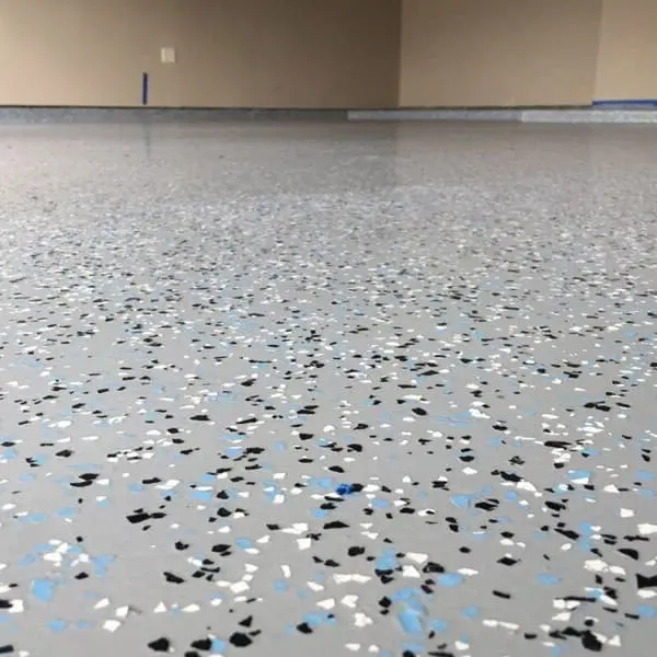 Close-up of light gray epoxy garage floor coating with decorative black, white, and blue color flakes.