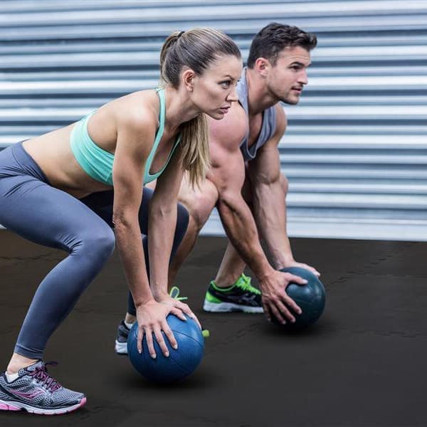 Home gym with Premium HD Soft Foam Tiles in black under two people exercising with medicine balls