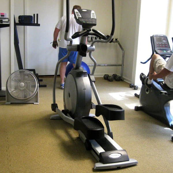 Man riding the indoor bike at the gym on tan interlocking rubber tiles.