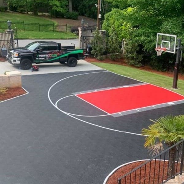 Outdoor basketball court with VersaCourt Active Tiles in black and bright red, featuring white court lines and a hoop
