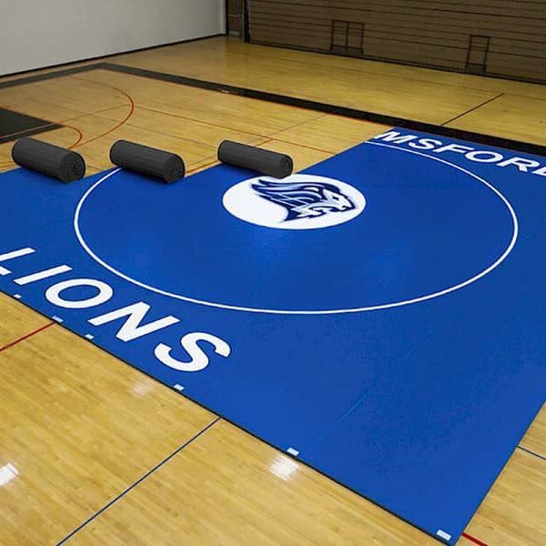 Wrestling mats in school gymnasium being rolled up.