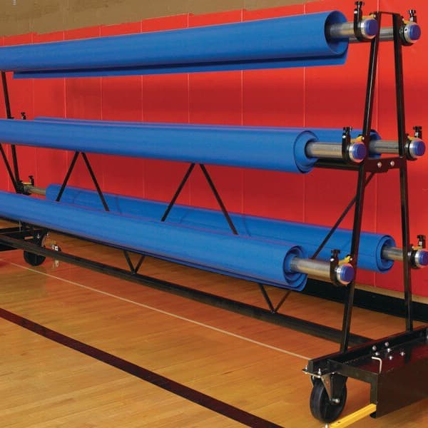 Mobile storage rack with three blue rolled mats on wheels, in a gym with hardwood flooring and red walls