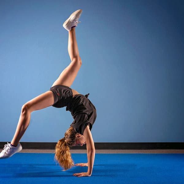 Girl performing handstand on blue Home Cheer Mat in gym setting