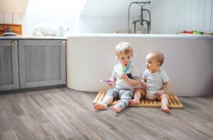 Two small children sitting in front of bathtub and on the floor. Featuring our Mohawk Versatech Plus 13' 2" Vinyl Sheet.