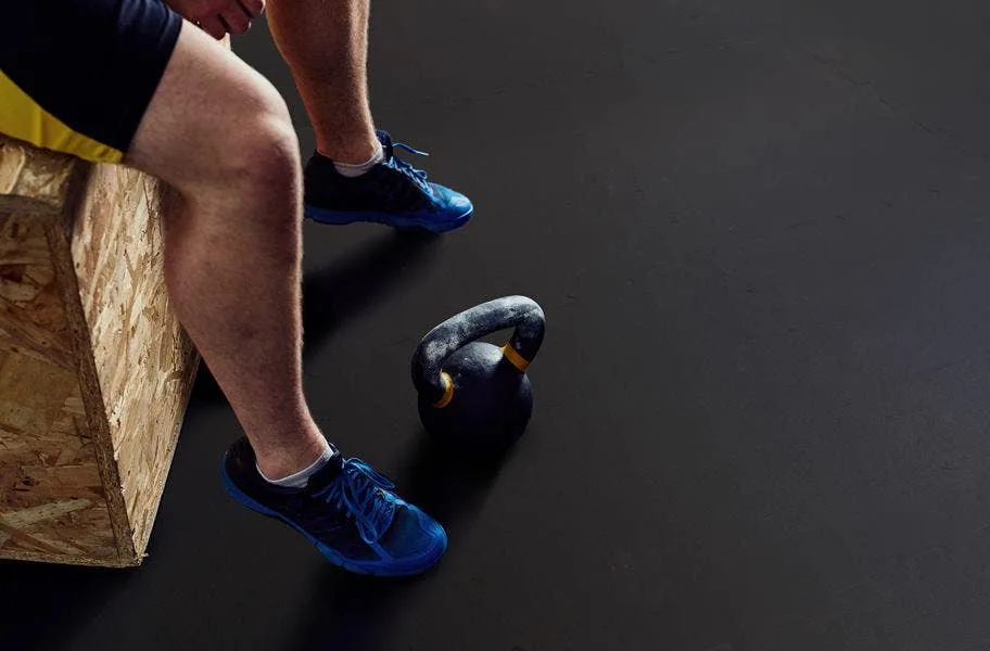 Athlete seated on a plyo box beside a kettlebell on black rubber flooring