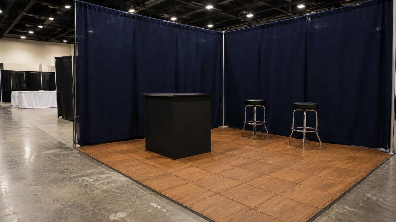 Trade show booth with wood-look interlocking foam floor tiles beside a bare concrete convention hall aisle