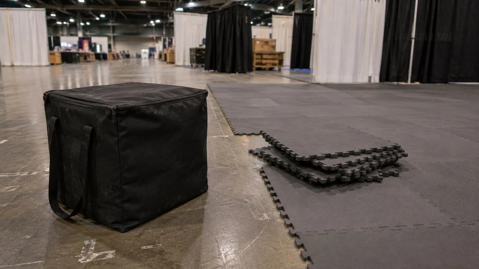 Soft carrying case for floor tiles on convention hall concrete next to a partially assembled interlocking tile floor