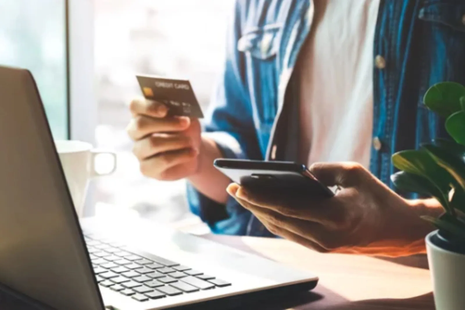 Secure online shopping and checkout Close-up of a person holding a credit card and a smartphone while shopping online at a laptop, illustrating easy and secure online checkout.