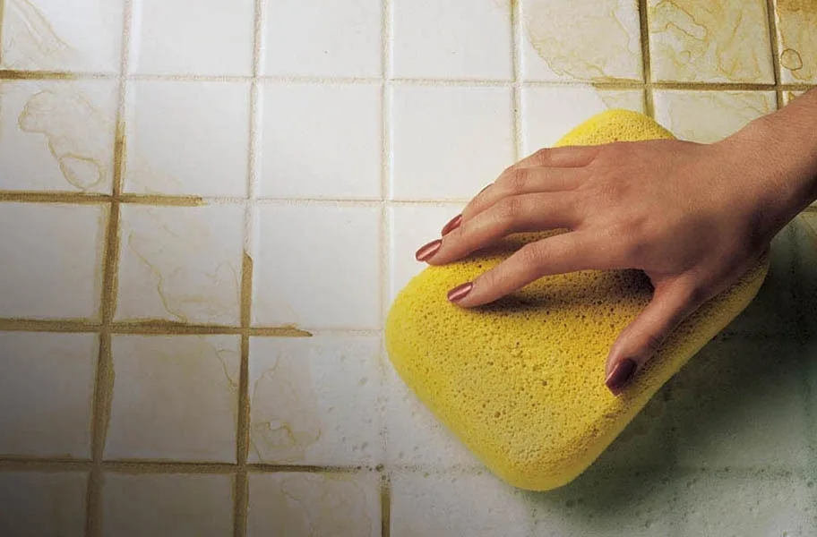 Hand scrubbing stained white tile grout with a yellow sponge
