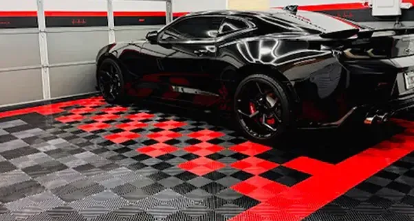 Red and Black Interlocking Garage Tiles A glossy black sports car is parked in a garage on a highly customized interlocking garage floor. The durable garage tiles feature a bold red, black, and gray checkerboard pattern and a solid red border, creating a high-performance and visually striking a