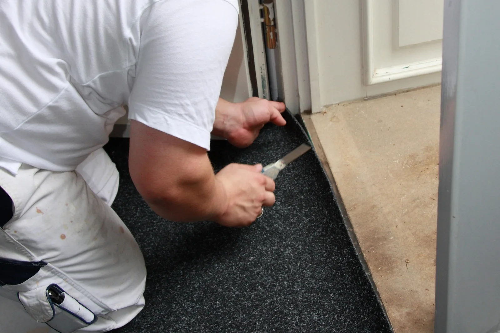 Installer trimming a rubber flooring roll along a door frame with a utility knife