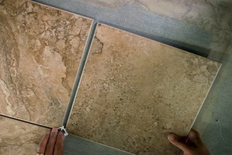 Dry-laying beige tiles with a spacer before setting them in mortar