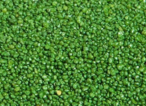 A close-up texture shot of green turf infill, showcasing the small granules used to weigh down and support the blades of artificial grass on sports fields and lawns.