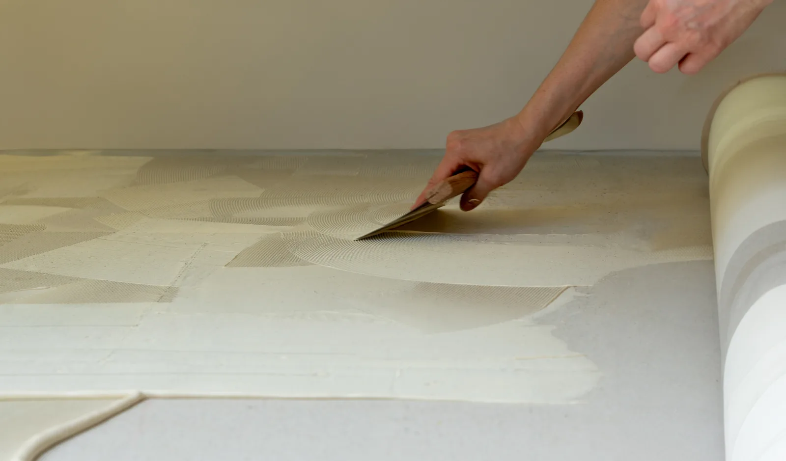 Spreading adhesive on a subfloor with a notched trowel beside a rolled-back floor