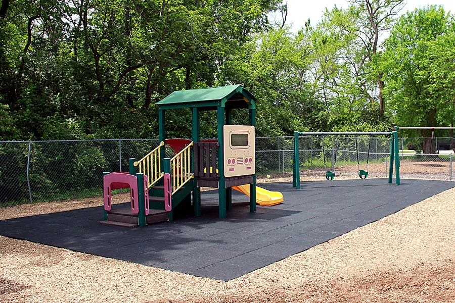 Black playground tiles over wood mulch with a commerical playground
