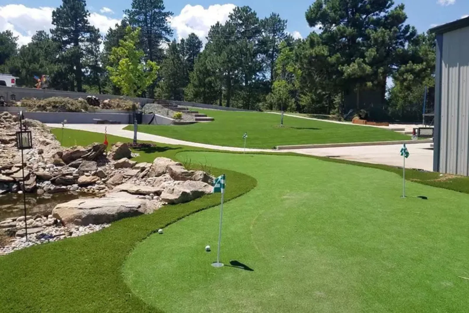Durable artificial turf putting green Outdoor putting green and tiered artificial grass landscaping with a waterfall feature, showcasing durable artificial turf for golf and landscaping.