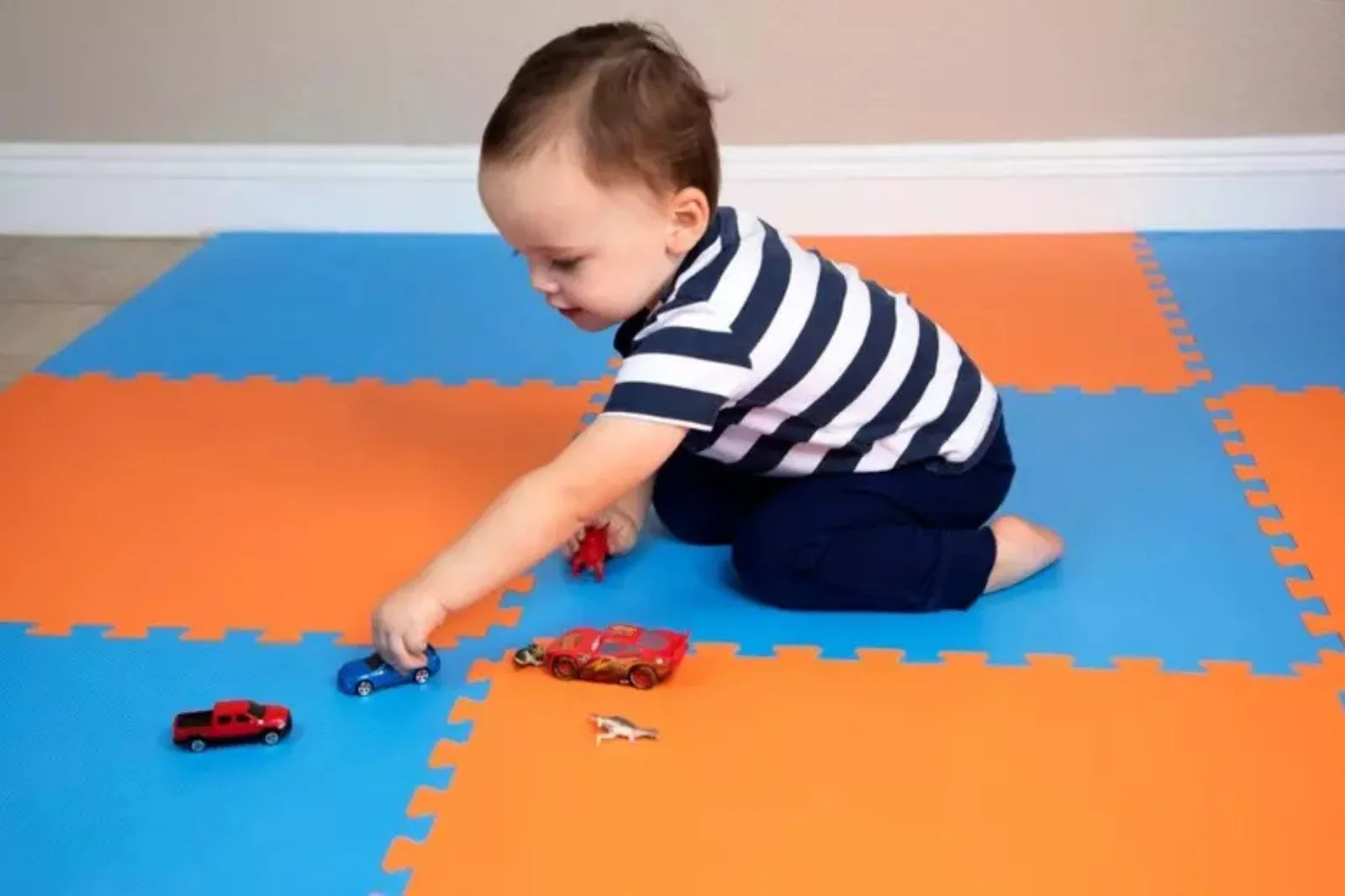 Durable interlocking foam floor tiles Toddler playing with toy cars on durable orange and blue interlocking foam floor tiles, providing a soft and colorful play surface.