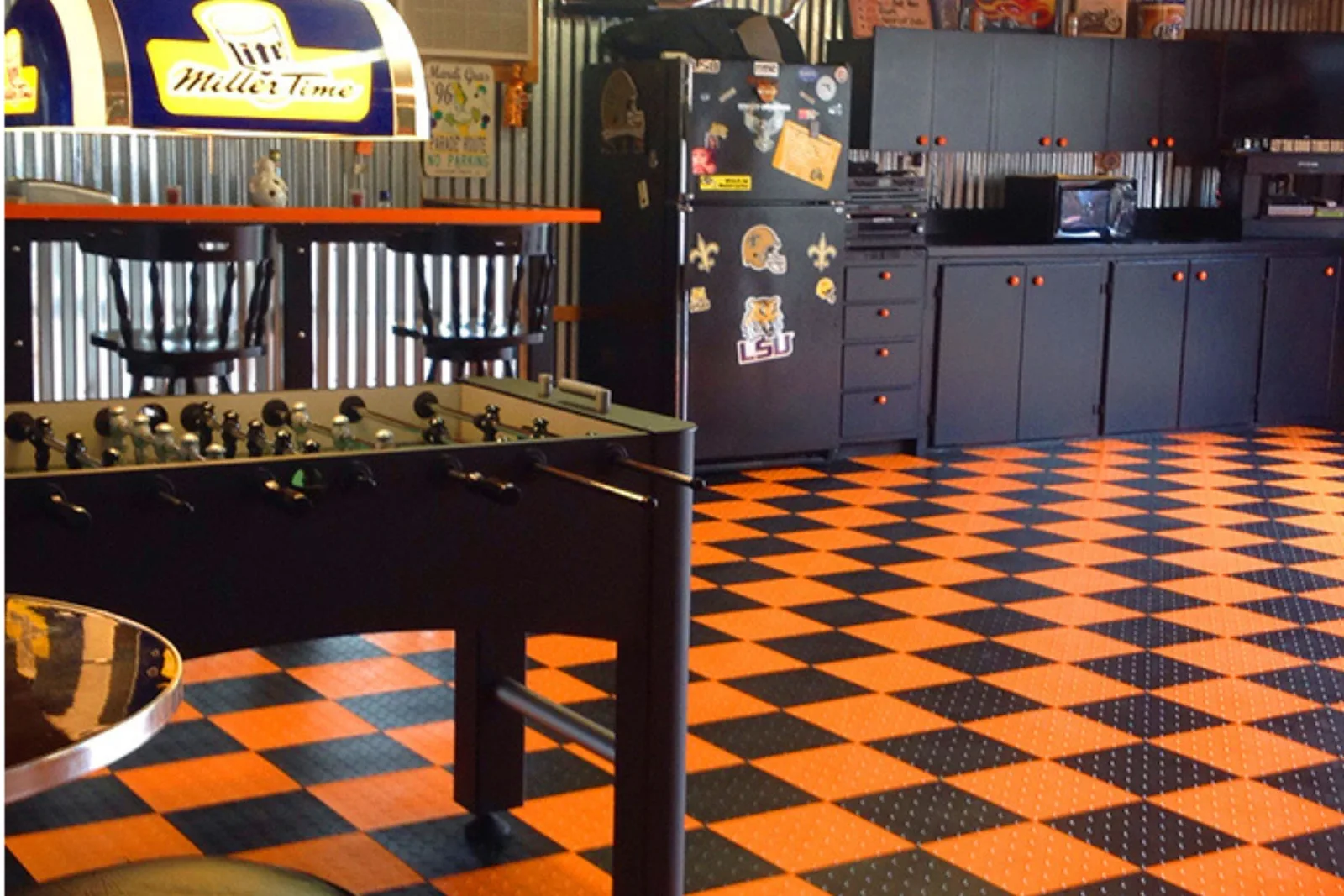 Checkered Garage Flooring Design High-contrast orange and black interlocking floor tiles in a basement game room with custom black cabinets and corrugated metal wall accents.