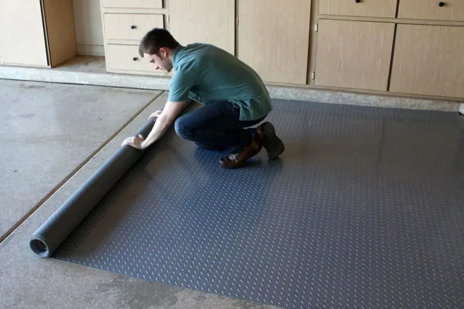 Man unrolling a gray diamond-plate garage flooring roll over concrete