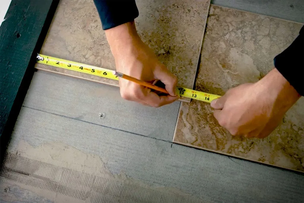 Measuring a ceramic floor tile while laying floor tile