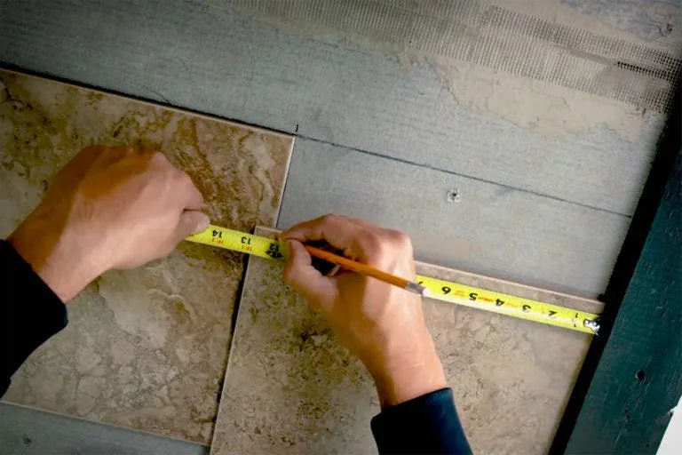 Measuring and marking a tile with a tape measure and pencil