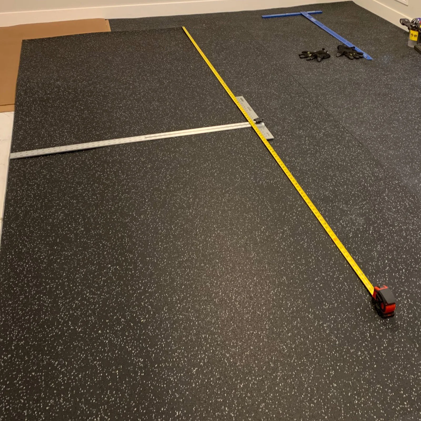 Tape measure and straight edges laid across black speckled rubber flooring rolls