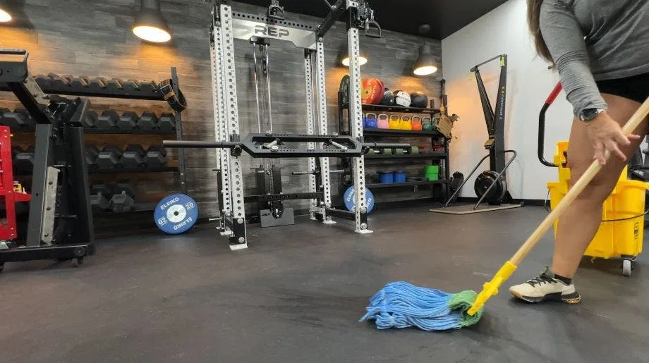 Mopping a black rubber gym floor in front of a power rack