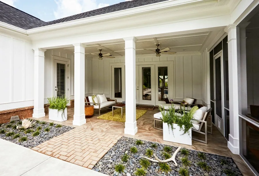 Covered patio with a brick paver walkway, river rock beds and white columns