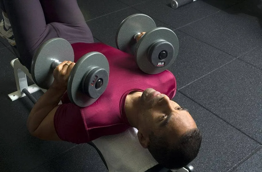 Man bench pressing dumbbells on black 1" sports play tiles
