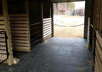 Black rubber stall mats covering the aisle floor of a wooden horse barn