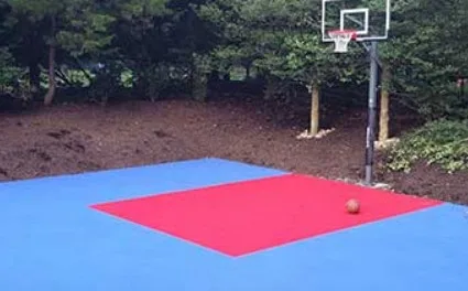 Outdoor basketball court tiles in blue and red, creating a low-maintenance, professional-looking, and durable court in a residential backyard.