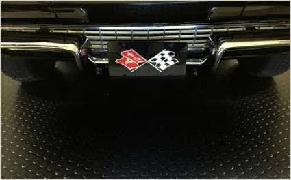 The chrome bumper of a classic black car with a checkered flag license plate is resting on black coin-top vinyl garage flooring. The roll-out garage matting provides a sleek, durable, and protective anti-slip surface for automotive display and maintenanc