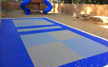 Outdoor sports tiles in a blue and gray checkered pattern, creating a durable and safe outdoor flooring solution for a multi-use court in a backyard.