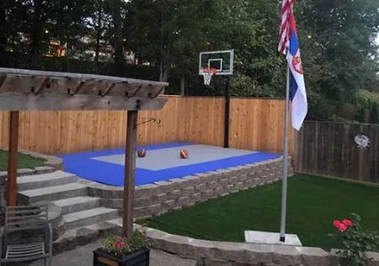 Outdoor court tiles for sports in a residential backyard, creating a low-maintenance, professional-looking, and safe playing surface with a basketball hoop and a flag pole.