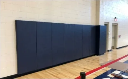 Blue foam safety wall pads installed in a traditional school gymnasium, providing a protective and cushioned barrier for athletes and students.