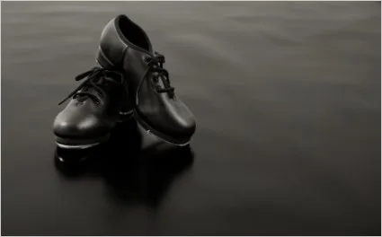 Pair of black tap shoes on a dark marley dance floor