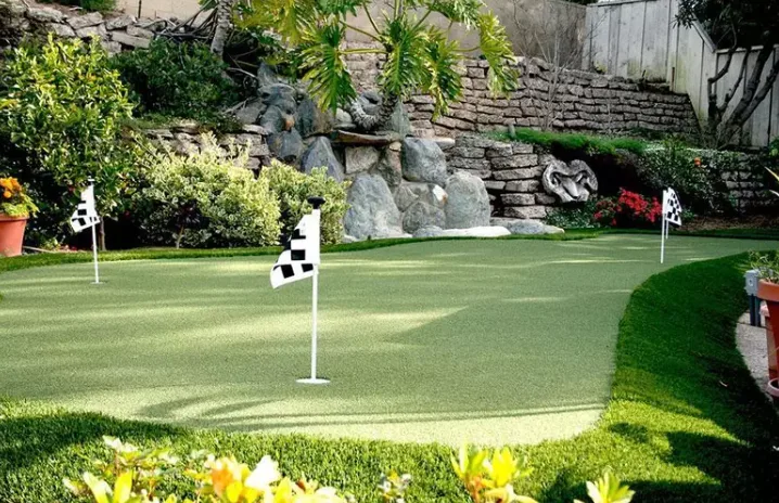 Putting green turf provides a low-maintenance and professional-looking surface for a backyard golf putting green with a flag and a golf ball.